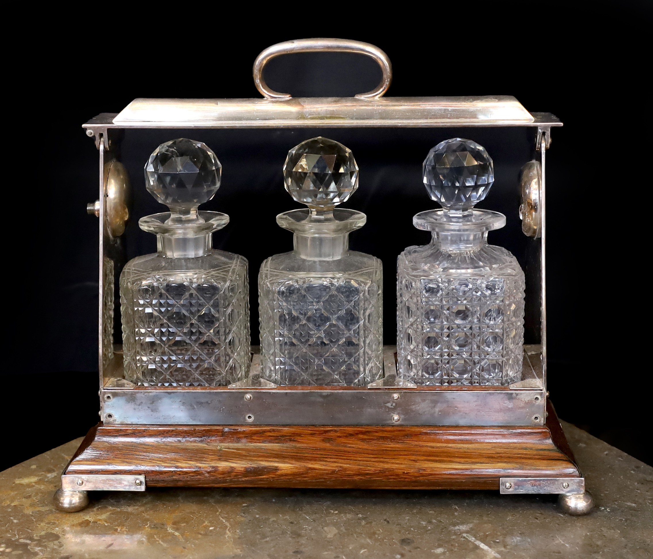 An Edwardian silver plated mounted oak tantalus fitted with three cut glass decanters, width 36cm
